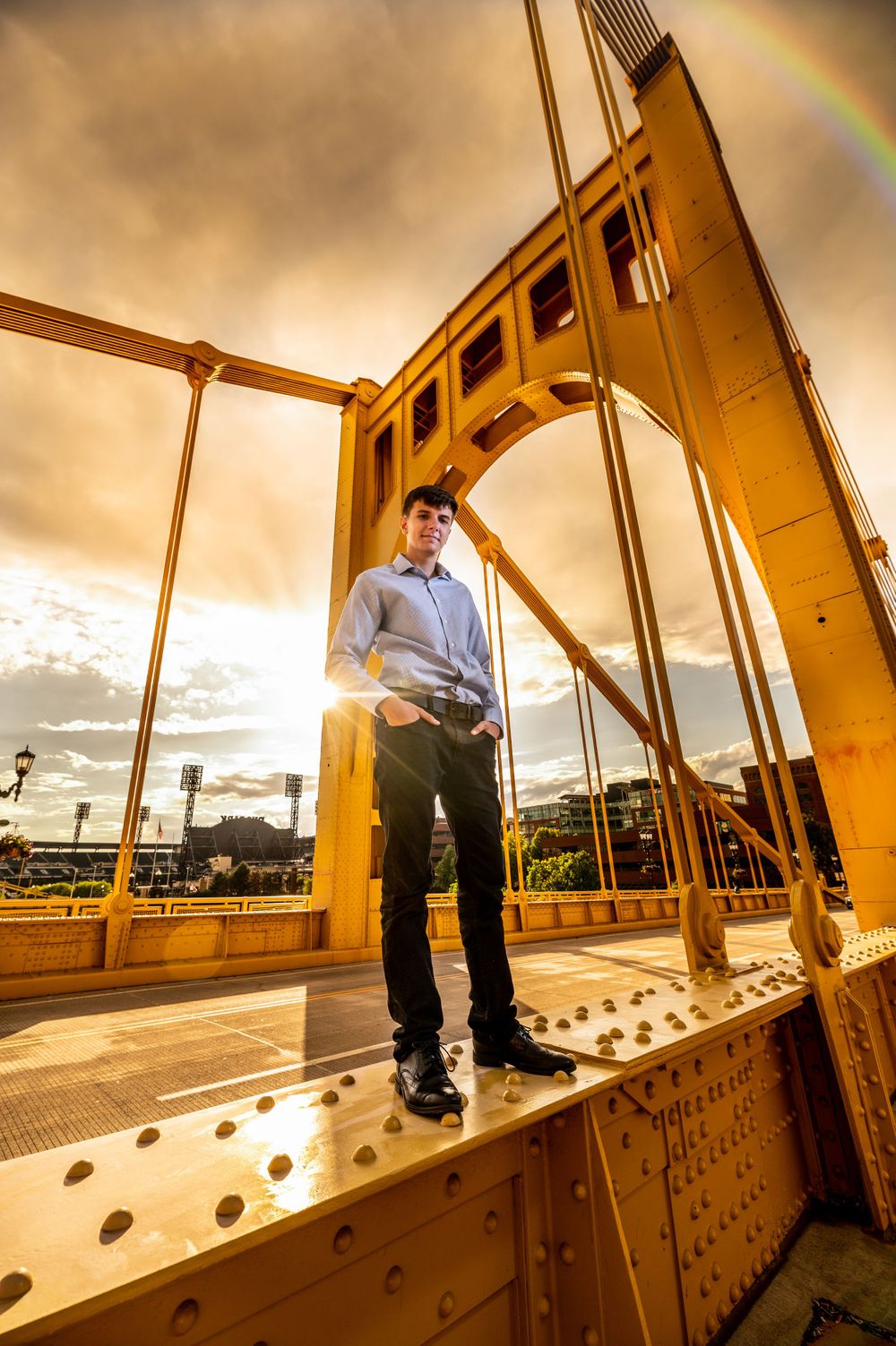 Dramatic sunset portrait on yellow bridge with rainbow in background.