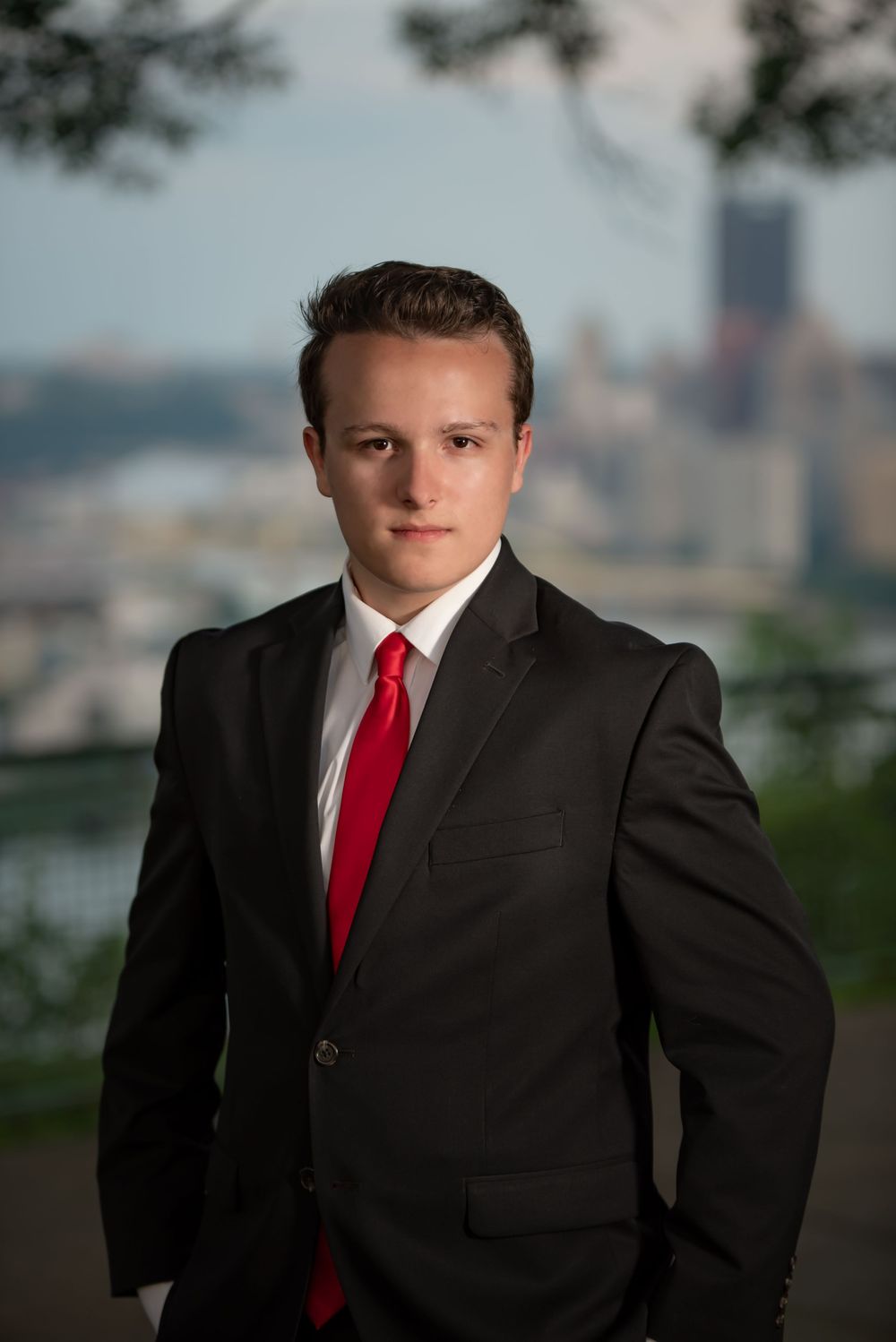 Business portrait with dark suit and red tie against city skyline.