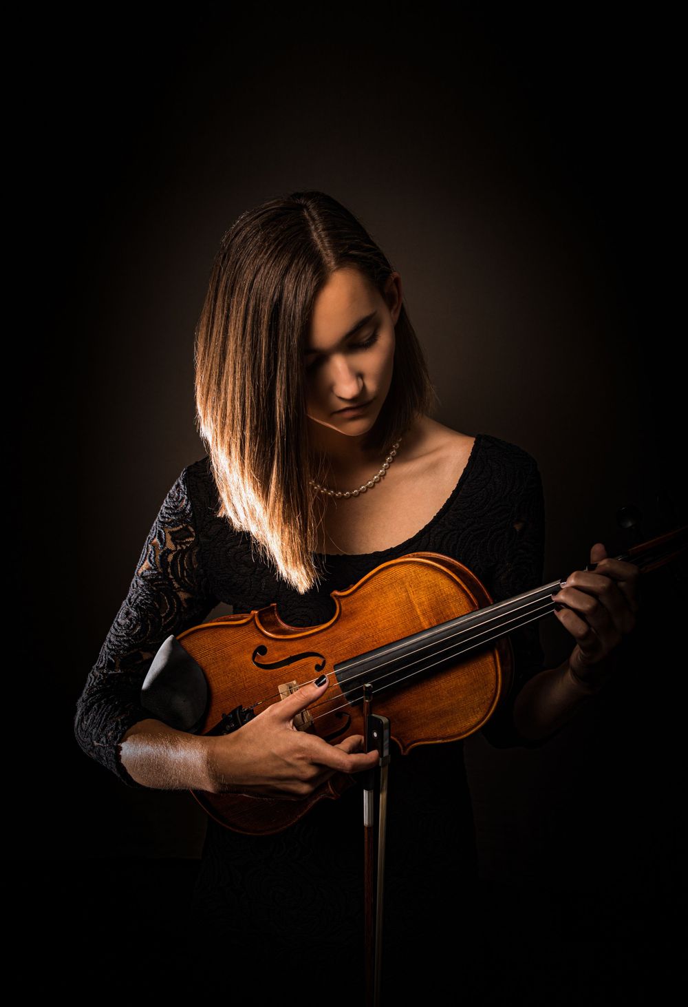 Dramatic low-key portrait of violinist with instrument in black dress.