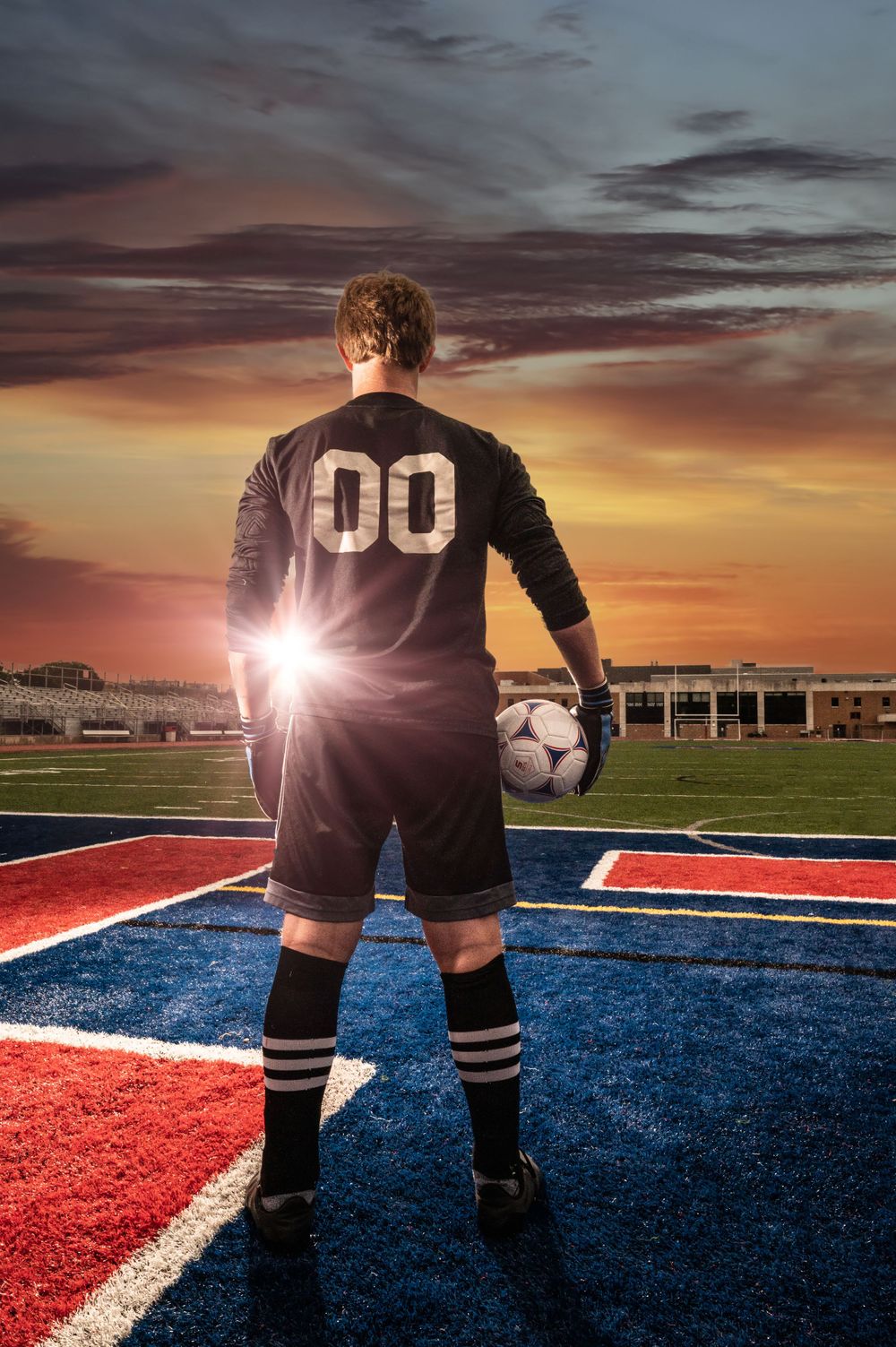 Soccer player in black jersey standing on field during dramatic sunset.