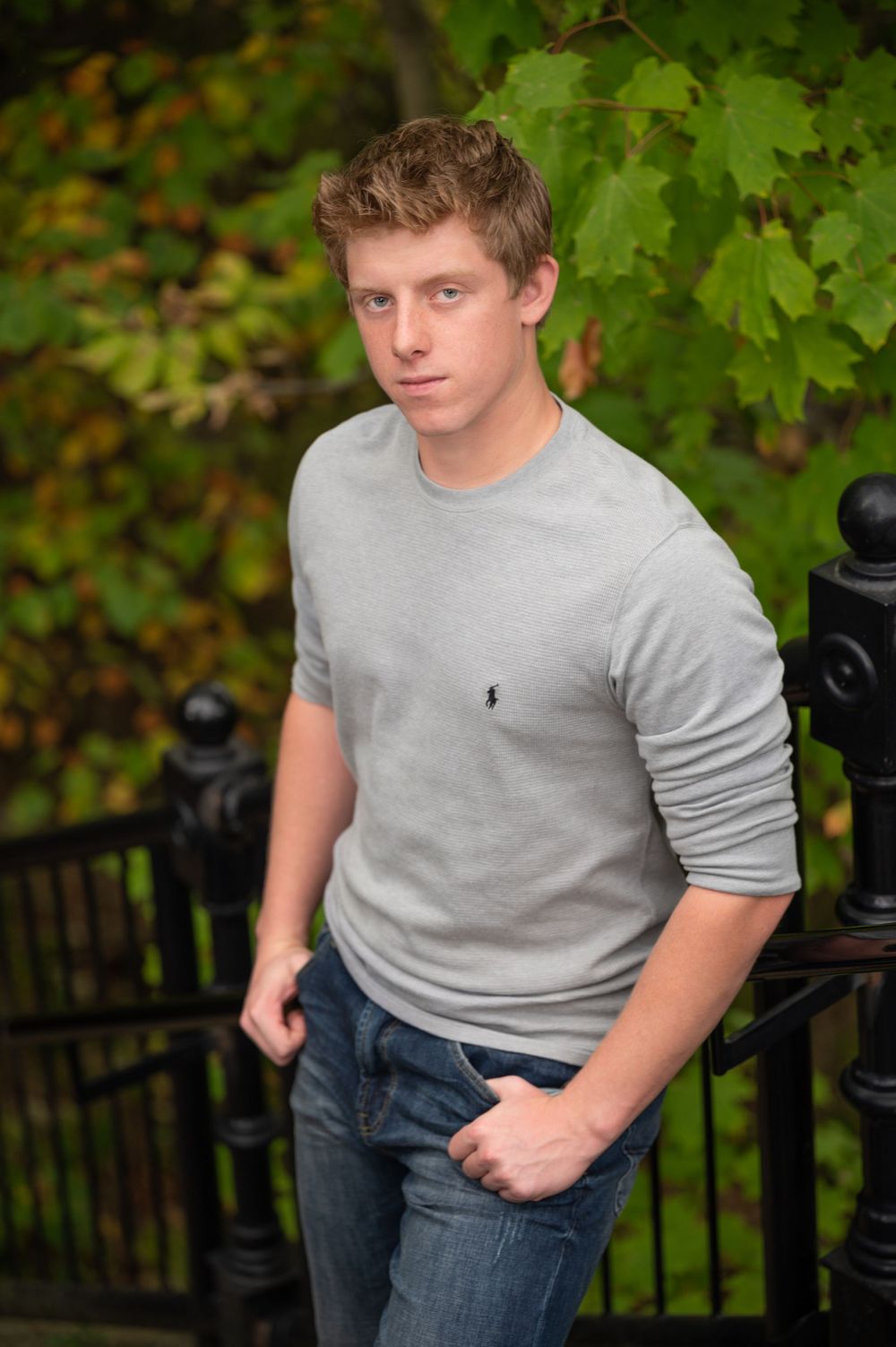 Portrait of person in gray sweater standing against fall leaves and iron railing.