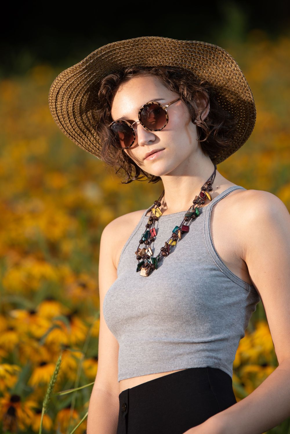 Summer fashion portrait in a flower field with straw hat and sunglasses.