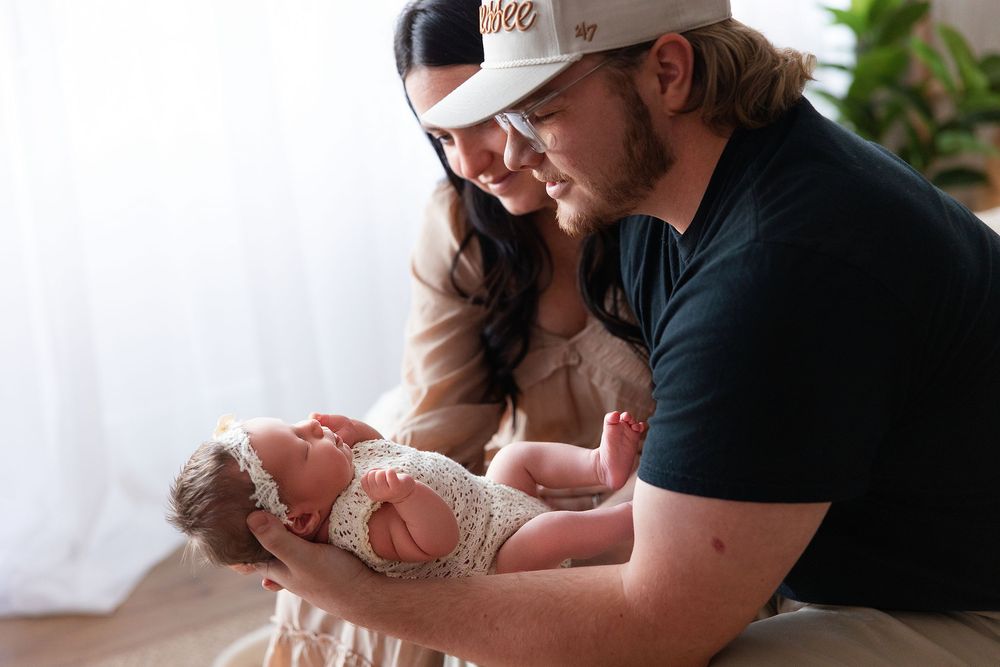 A tender moment as a parent in a baseball cap holds a newborn baby swaddled in white lace.