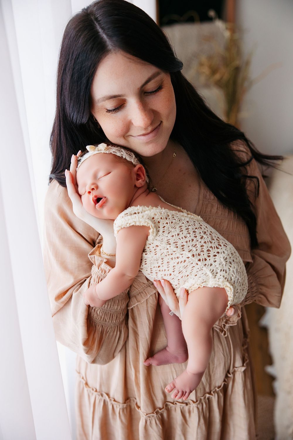 A tender moment between mother and baby wearing a crocheted white dress against a light background.