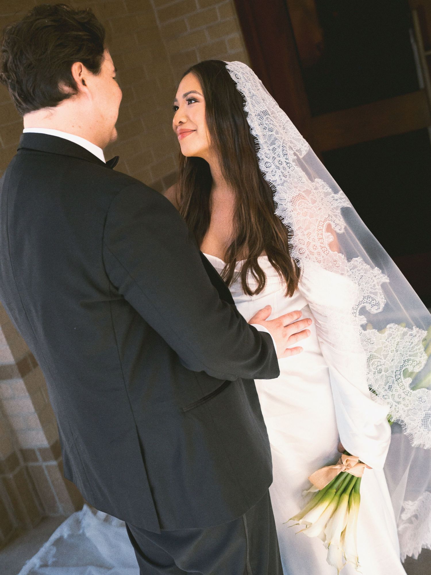 A romantic wedding scene showing a bride in white lace veil and groom in dark suit sharing an intimate moment.