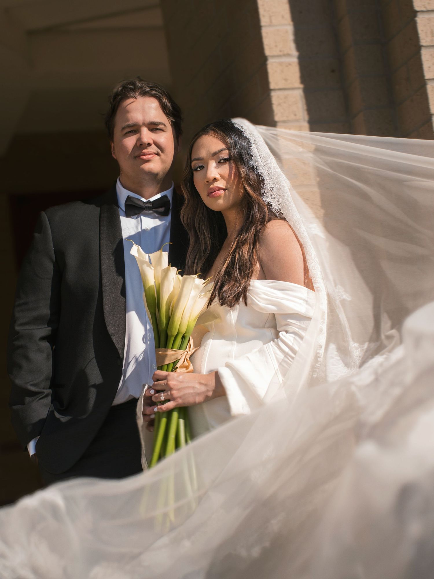 Sunlit wedding portrait with flowing veil and yellow calla lily bouquet.