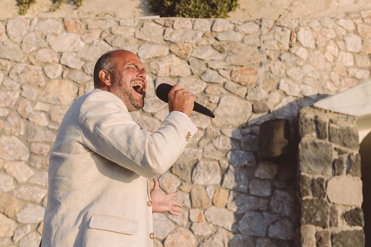 A man singing into a microphone at El Viento against a rustic stone wall backdrop.