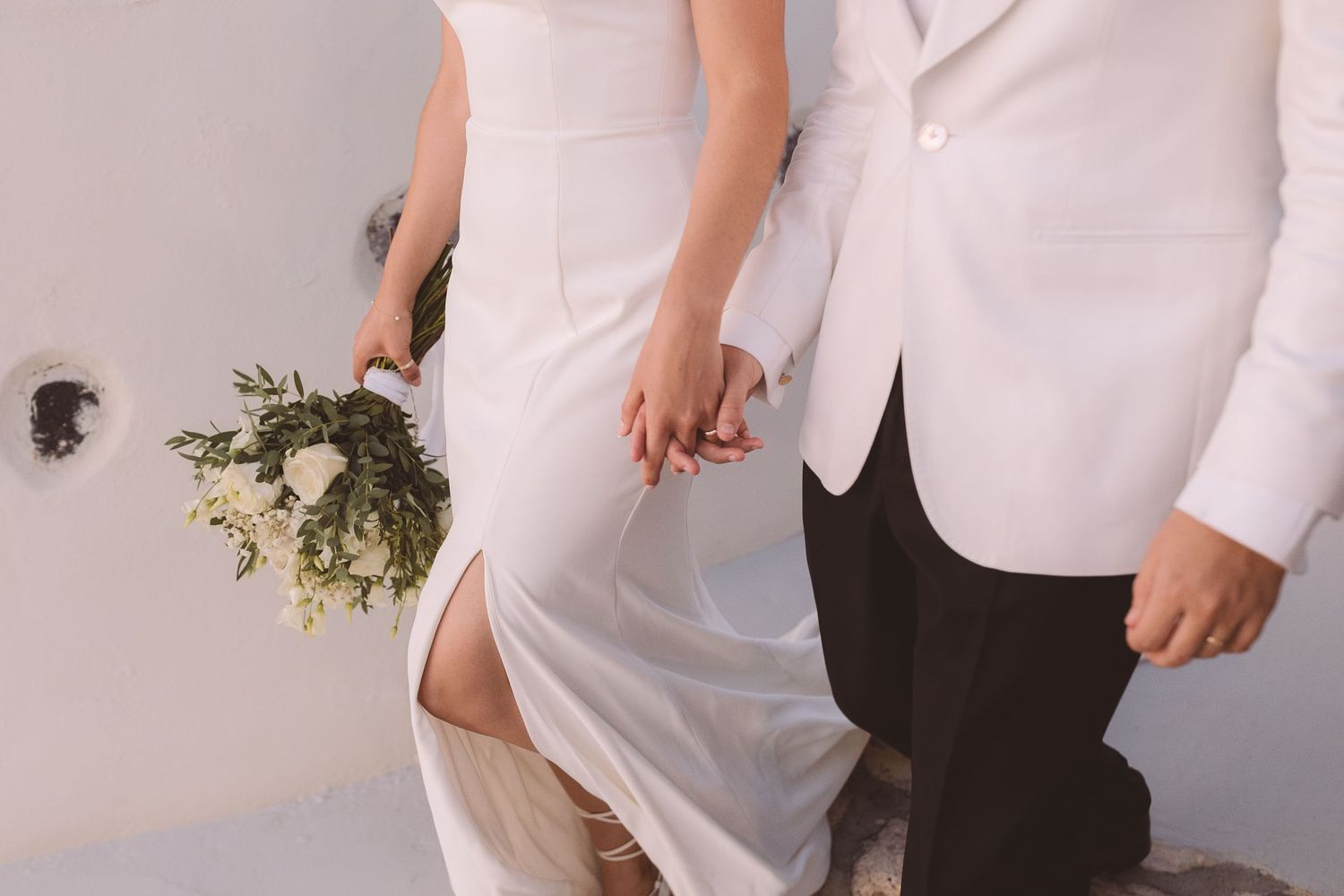 A destination wedding couple walks hand in hand at sunset at El Viento Santorini, Greece.