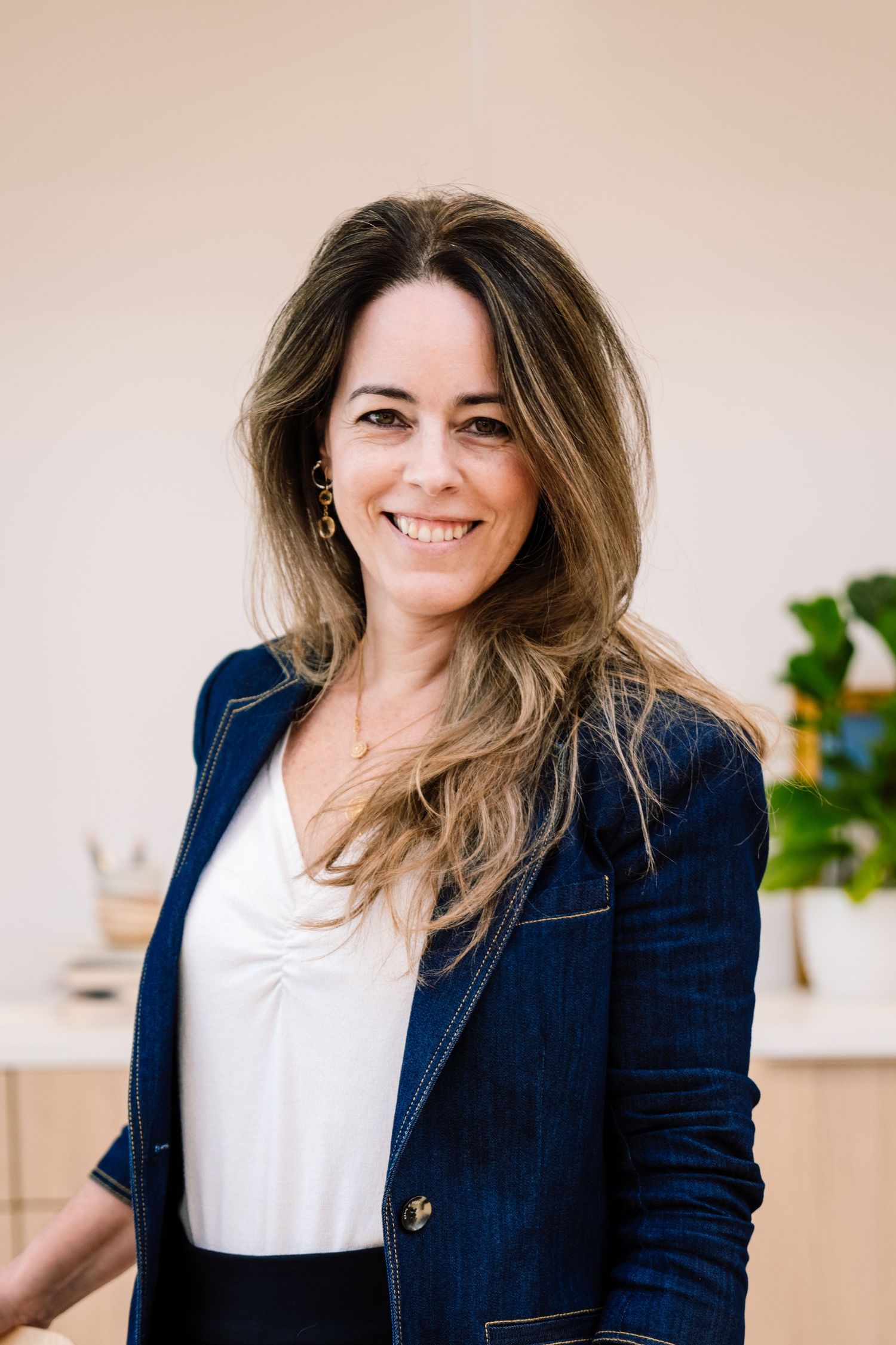 Professional wearing a navy blazer and white top poses in front of a light beige background.