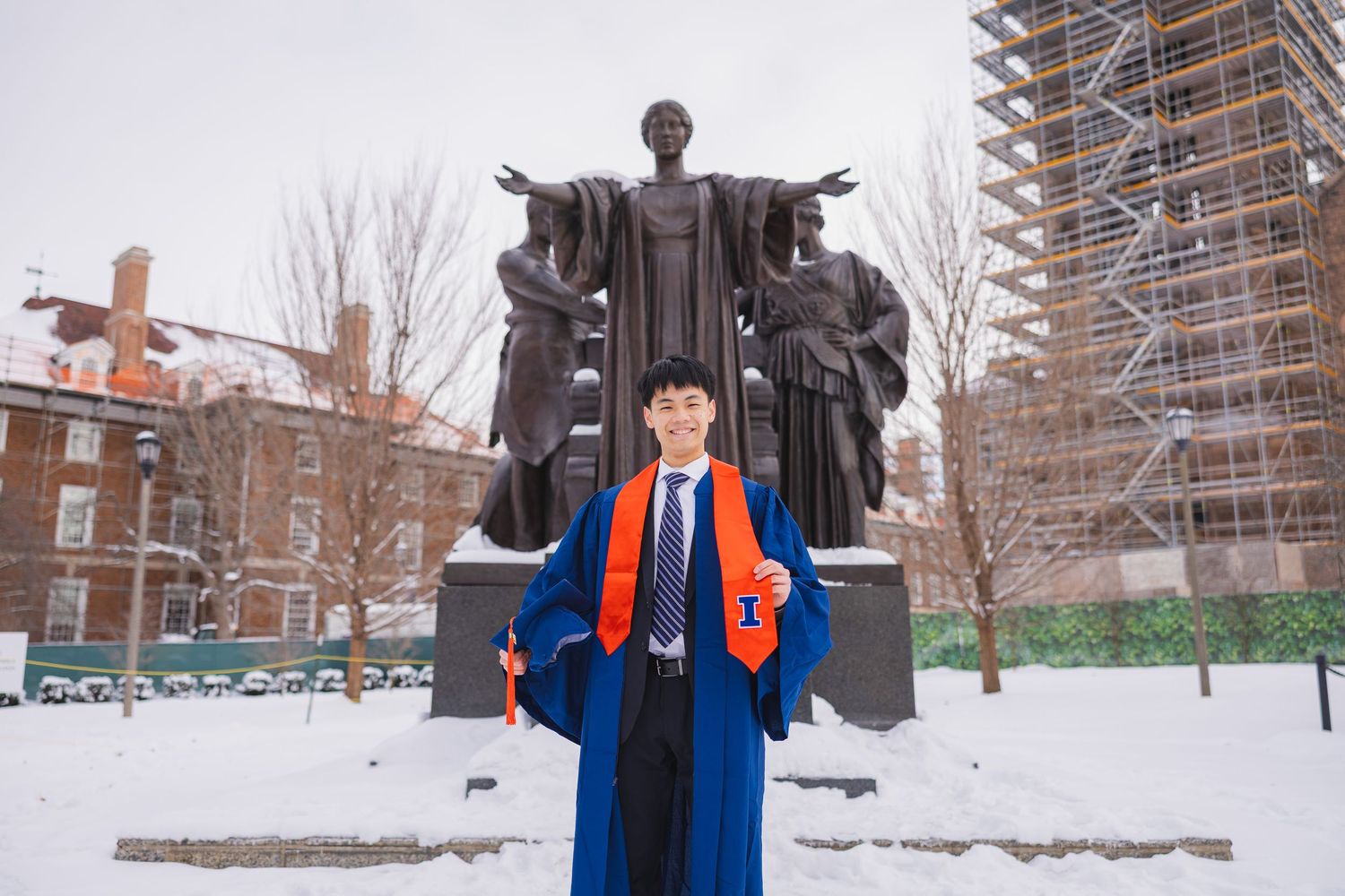 UIUC graduating student with cap and gown holding a University of Illinois stole in front of Alma Mater
