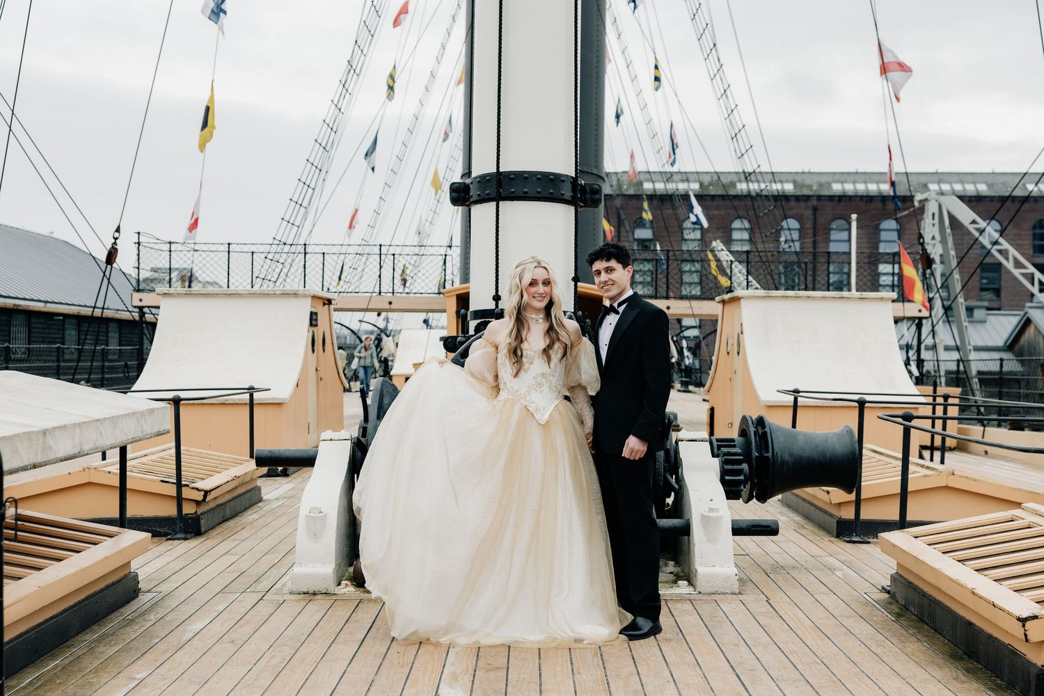 A couple shares an intimate moment on a cruise ship deck with flags waving in the background.