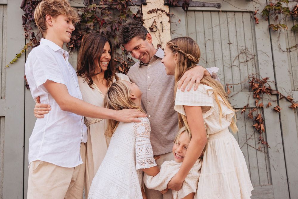 A joyful group wearing white outfits embraces and laughs together during an outdoor photo session.