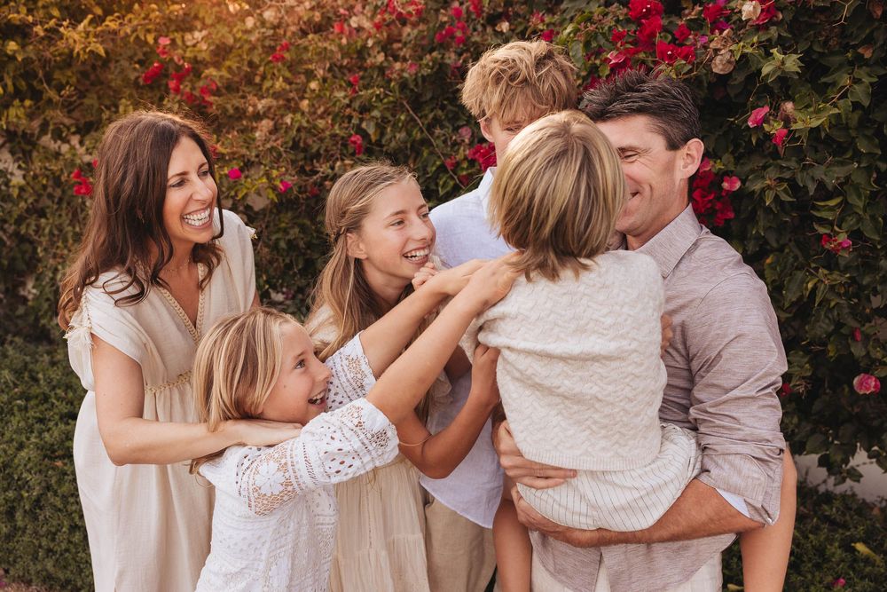 A family shares joyful moments together in front of blooming red bushes during an outdoor photo session.