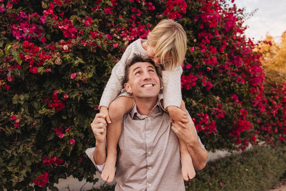 A couple embraces in front of vibrant pink bougainvillea flowers during a romantic sunset photoshoot.