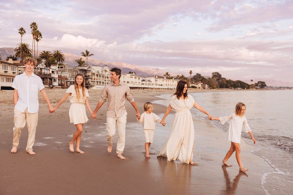 A group of people in white outfits walking along a beach at sunset with palm trees in the background.