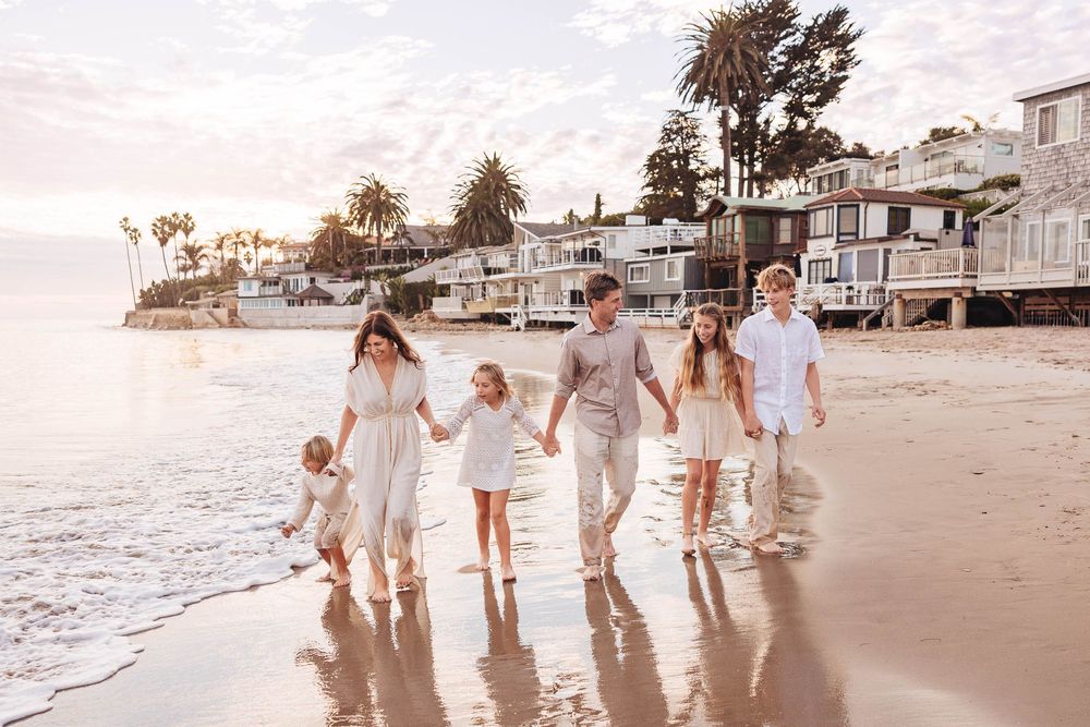 A family wearing white outfits walks along a sandy beach at sunset creating a dreamy coastal scene.