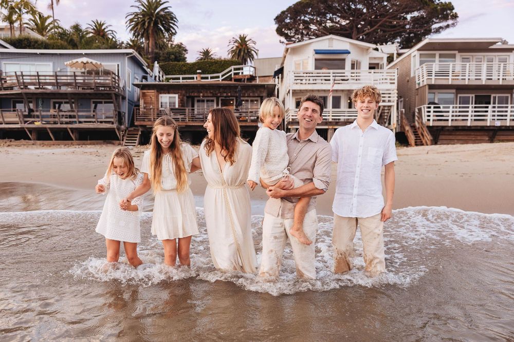 A group in white outfits walking along a sandy beach at sunset with palm trees in the background.