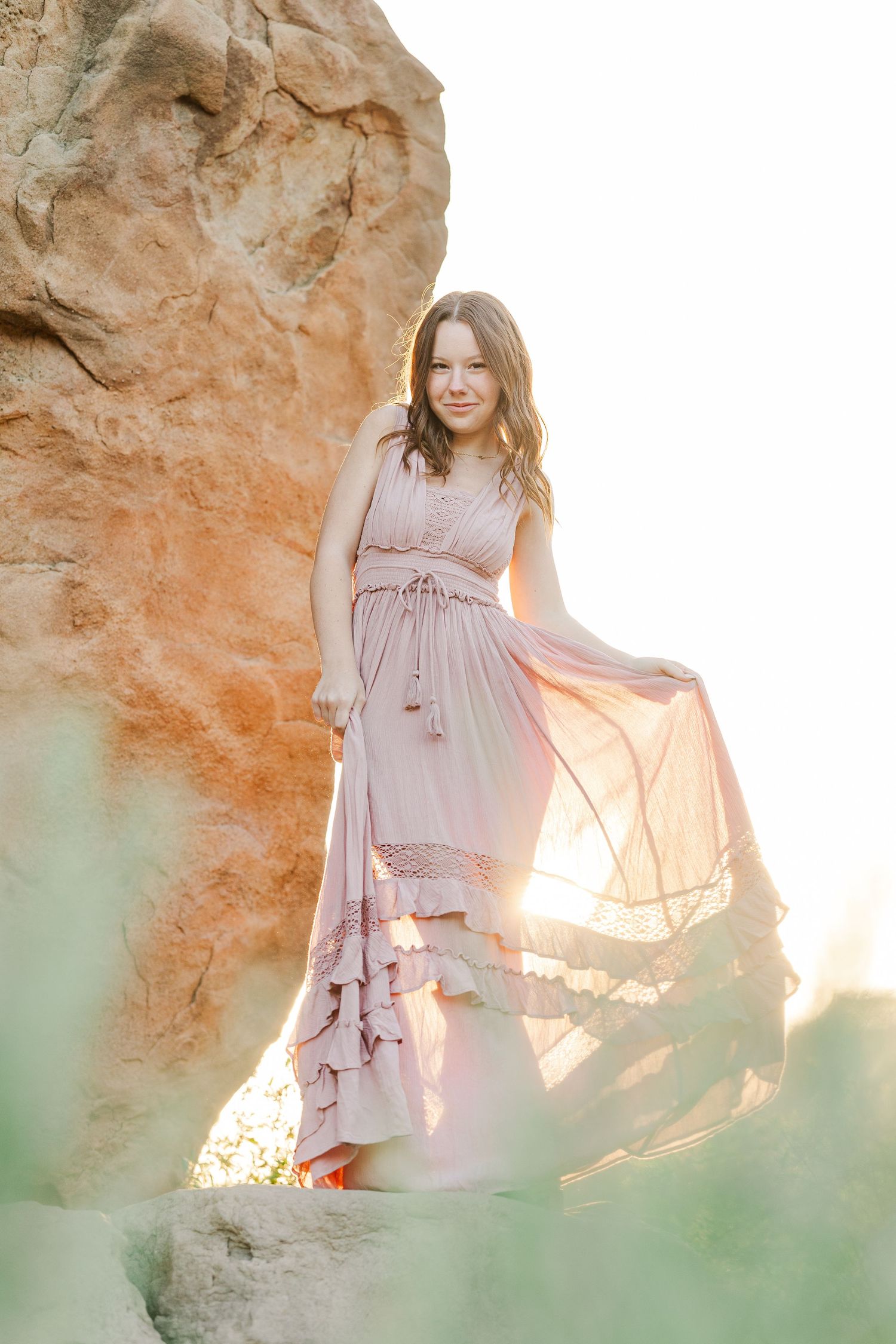 Ethereal outdoor maternity photo series showing a flowing pink dress against golden sunlit rock formations.