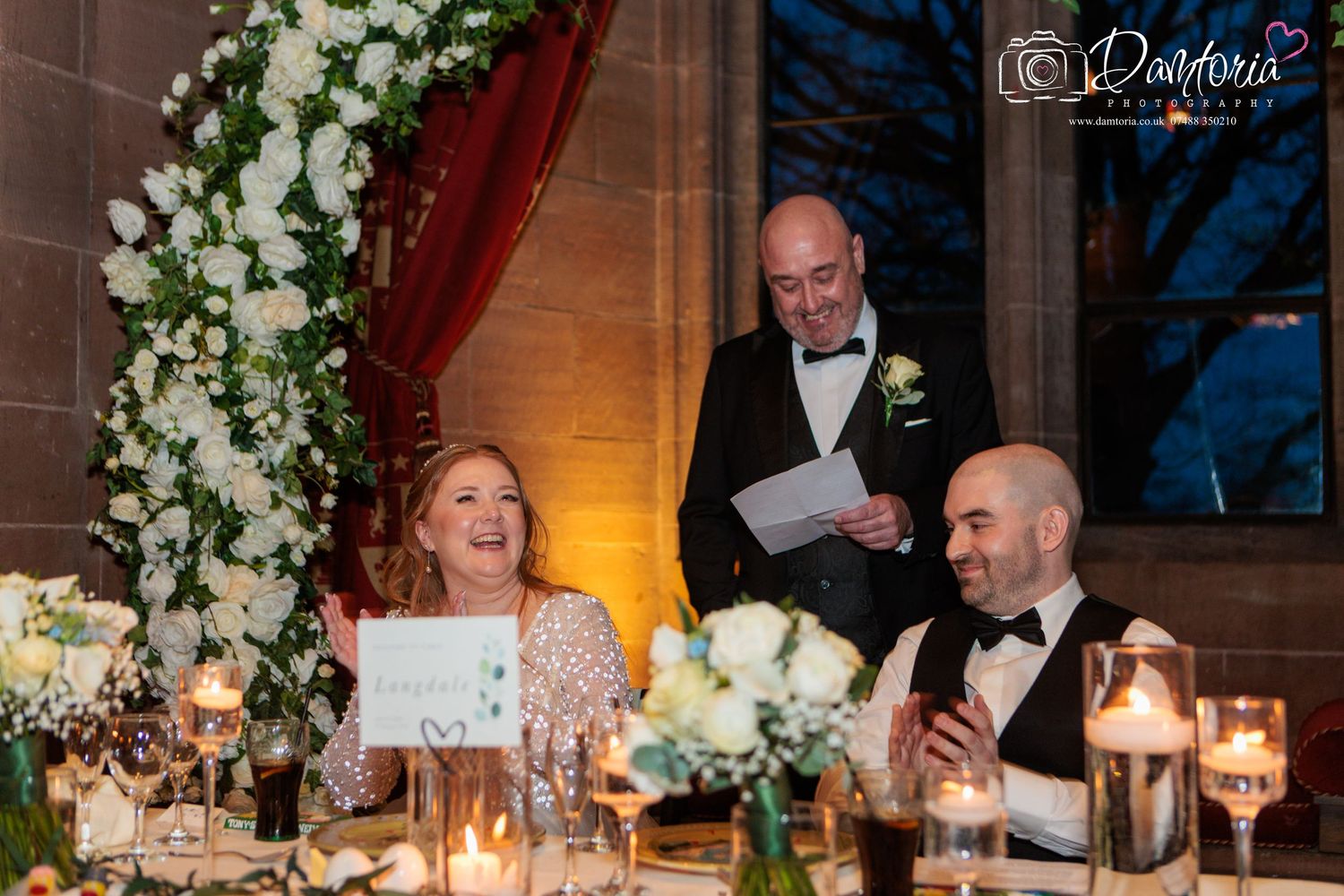 Elegant wedding reception dinner table decorated with white floral centerpieces and glowing candlelight.