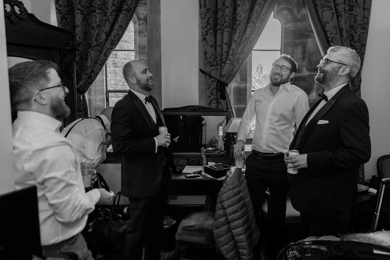 A black and white photo shows a group of men in formal attire having an animated conversation in an interior setting.