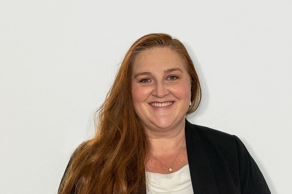Professional headshot of someone wearing a black blazer against a light background.