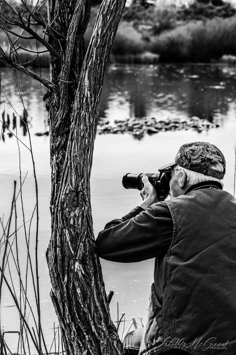 Black and white silhouette of a photographer by a lake capturing reflections in nature.