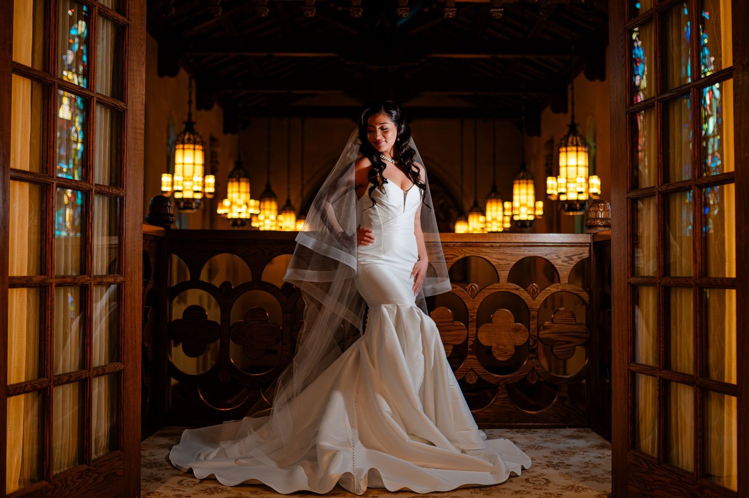 A bride and groom pose in an elegant hallway with warm lighting and ornate wooden details during their wedding.