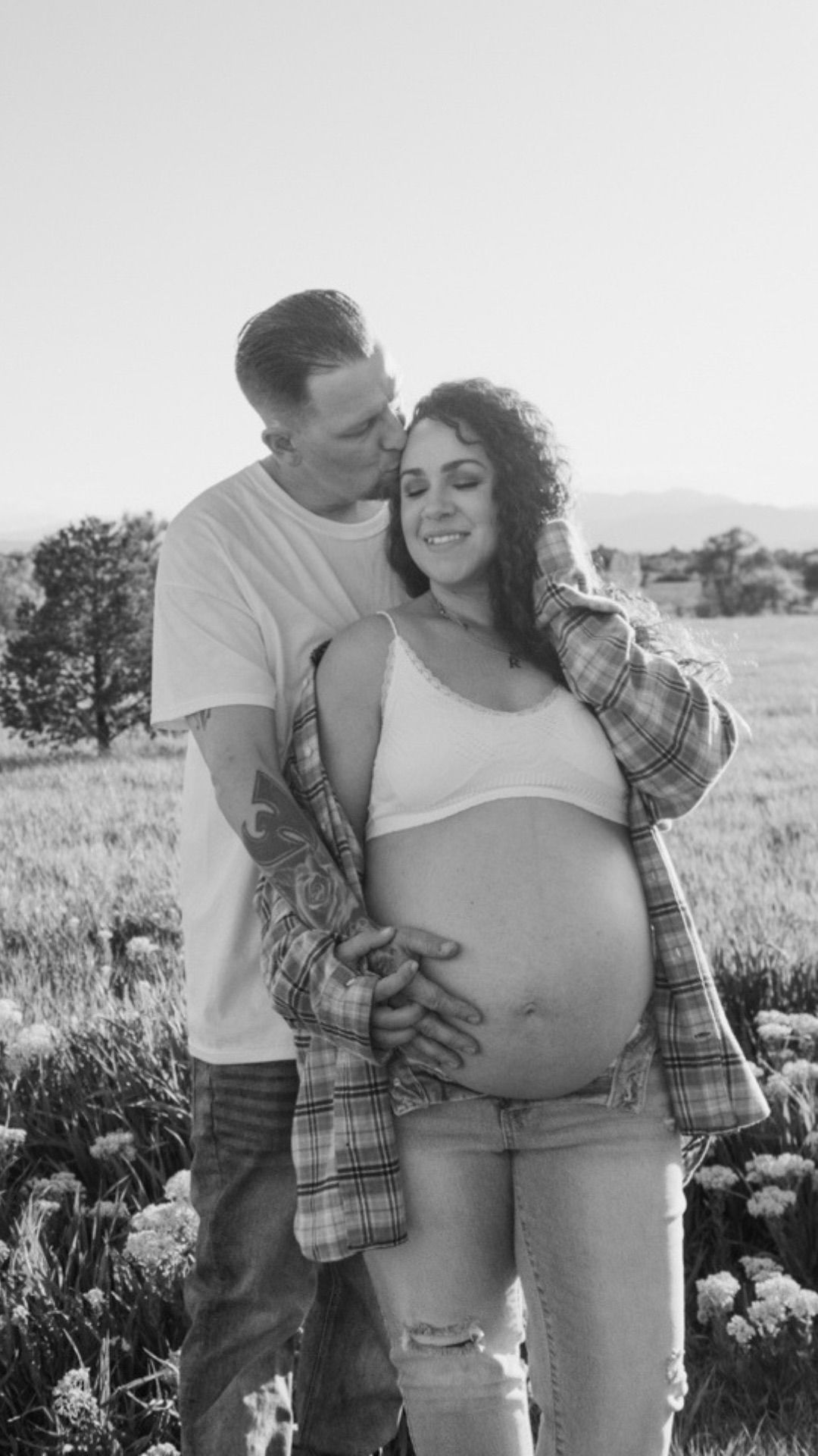 Black and white photo of couple in a field man kissing woman's head while holding her baby bump | Westminster maternity photos
