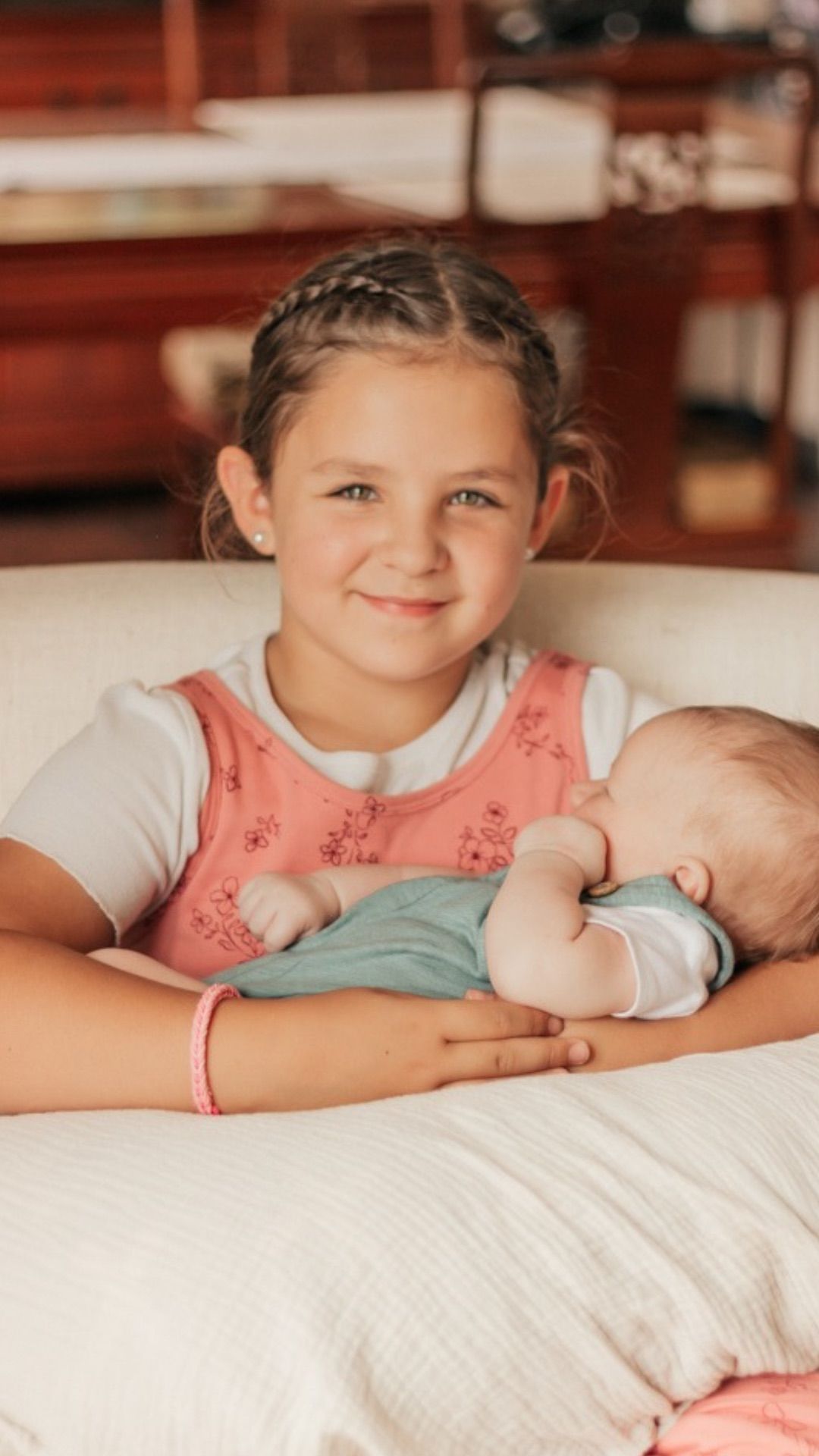 Young girl with braided hair gently holding a sleeping newborn baby on a white couch | newborn photographer Arvada Colorado
