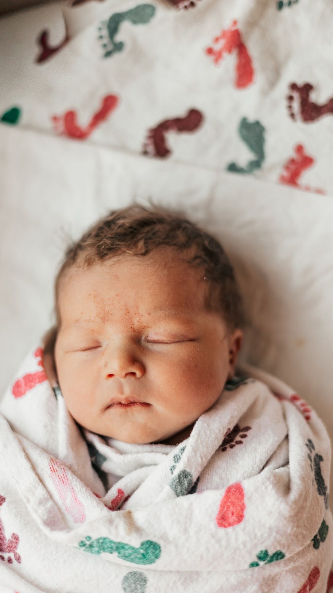 Sleeping newborn wrapped in a white blanket with colorful dinosaur prints.