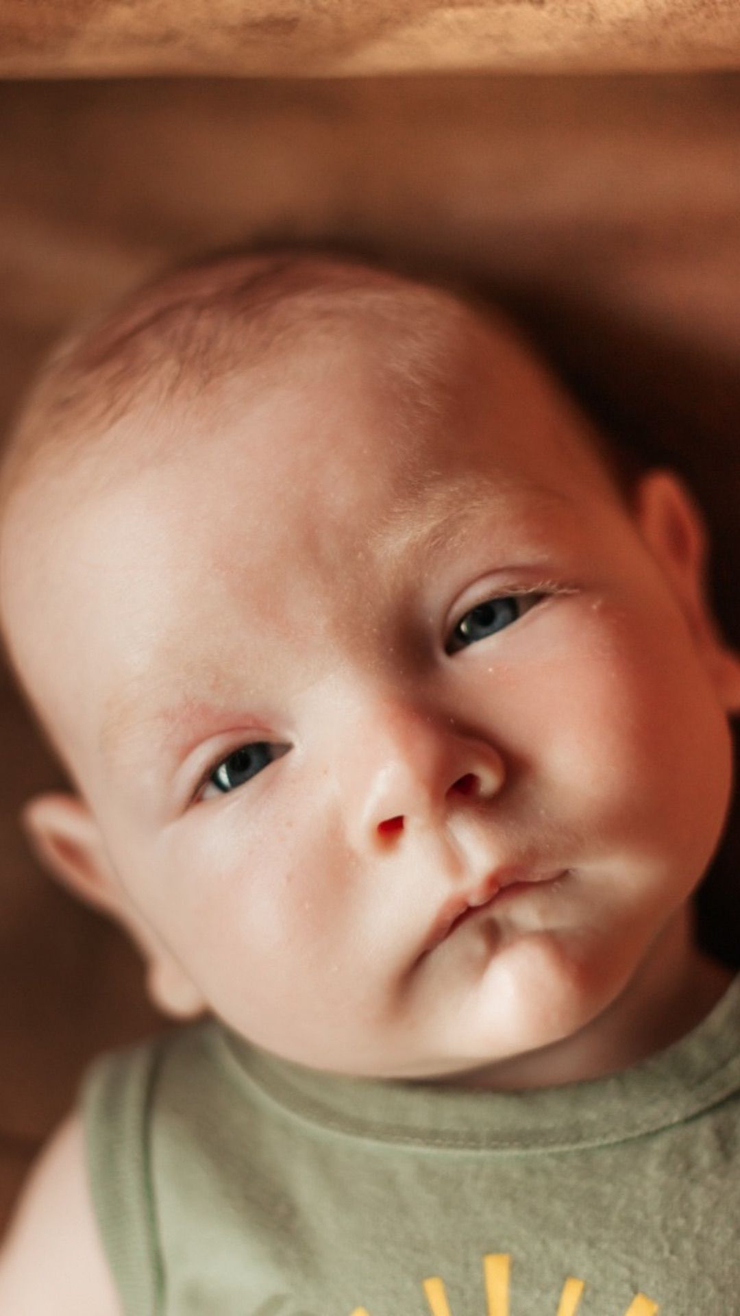 Close-up portrait of curious blue-eyed baby in green onesie looking up | Westminster Colorado childhood photographer