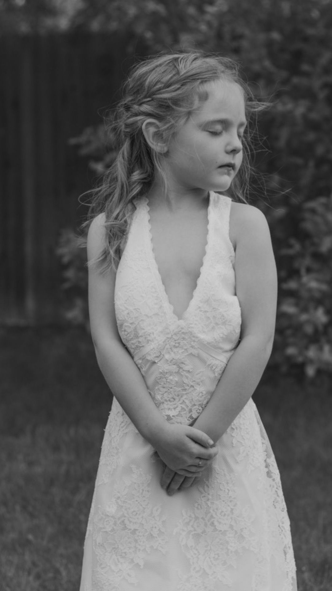 Black and white photo of young girl in white lace dress eyes closed and hands clasped outdoors | children's photographer Westminster CO