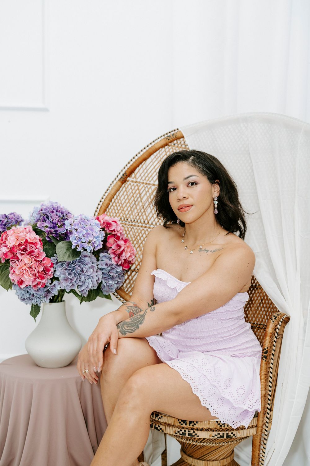 Romantic boudoir photo shoot featuring pink lingerie, wicker peacock chair and floral arrangements.