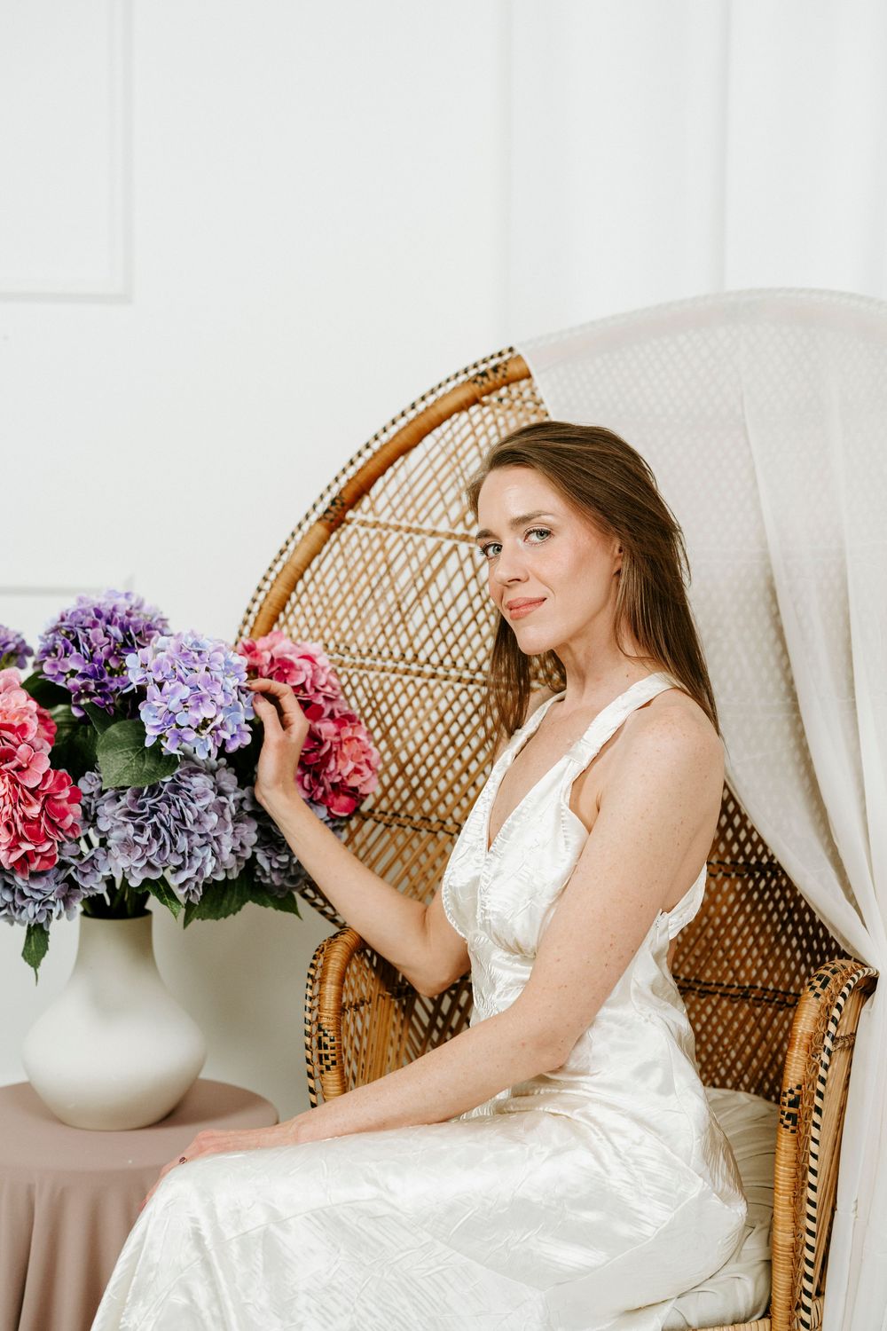 Dreamy bridal photos with white dress, wicker chair and pink and purple floral decorations.
