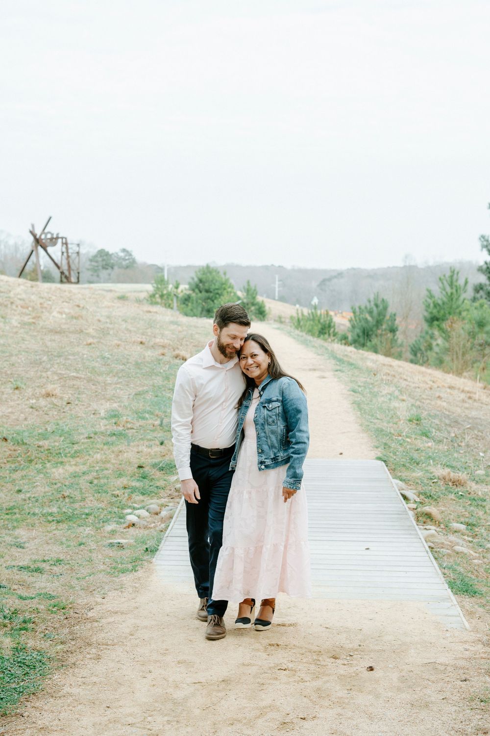 A couple walking together on a wooden boardwalk path through a grassy hillside on a cloudy day.