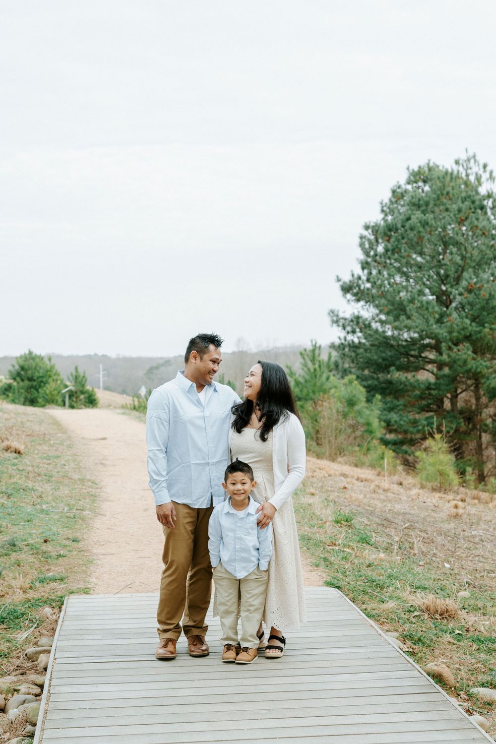 A family walks together on a wooden boardwalk path through a scenic natural hillside landscape.