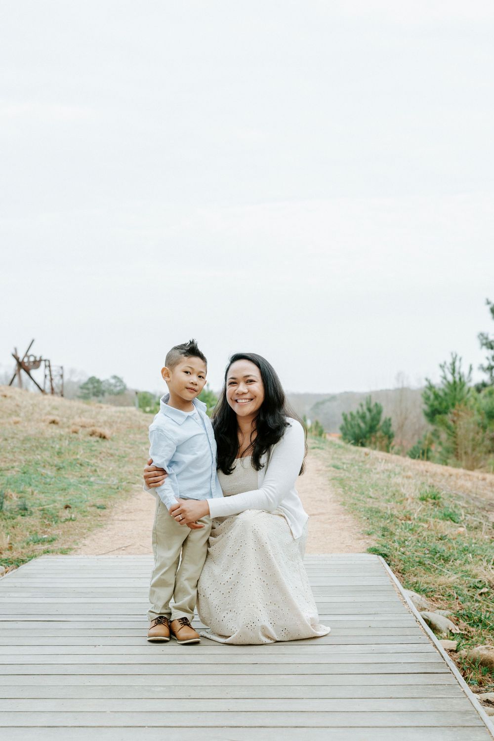 A parent and child share a tender moment while sitting together on wooden steps in a natural outdoor setting.