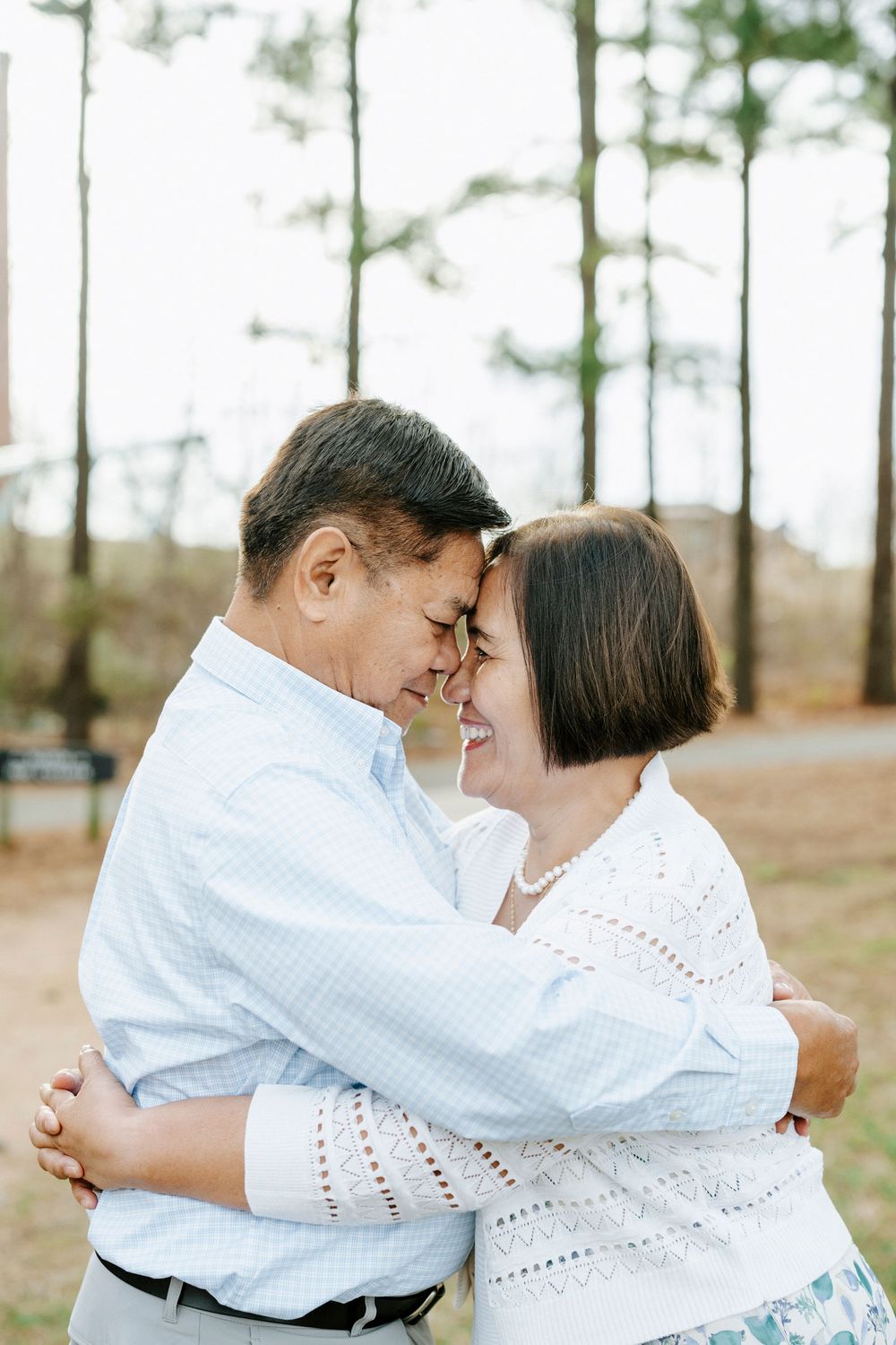 A romantic couple embracing and sharing an intimate moment outdoors among tall pine trees.