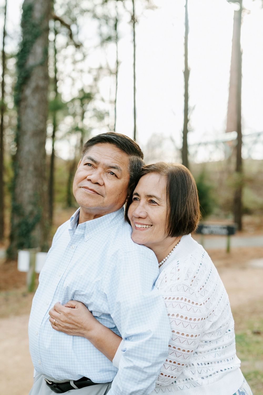 A couple wearing white embraces lovingly in an outdoor wooded setting during a photo session.