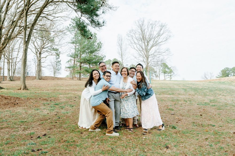 A group poses together outdoors on a grassy hill with bare trees in the background during a sunny day.