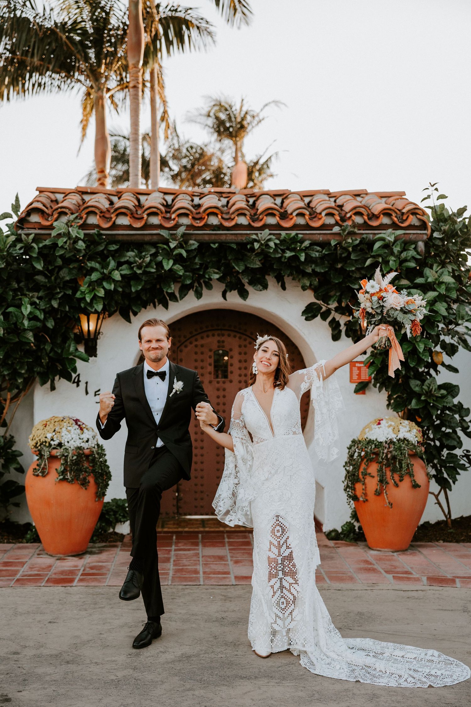 Joyful newlyweds celebrate outside a Spanish-style venue with terracotta roof tiles and lush greenery.