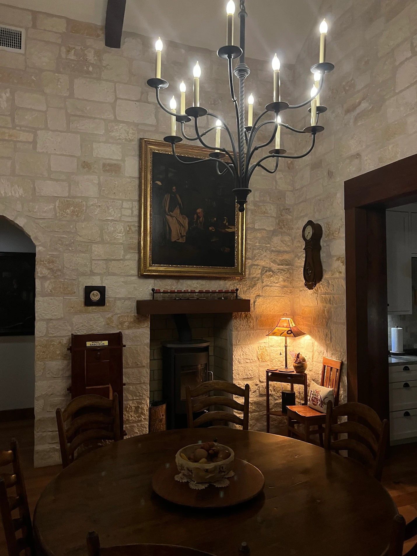 Rustic dining room with stone walls, wrought iron chandelier, and dark wood furniture illuminated by warm lighting.