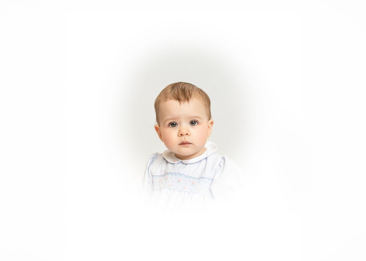 A baby wearing a gray sweater smiles while sitting against a white background.