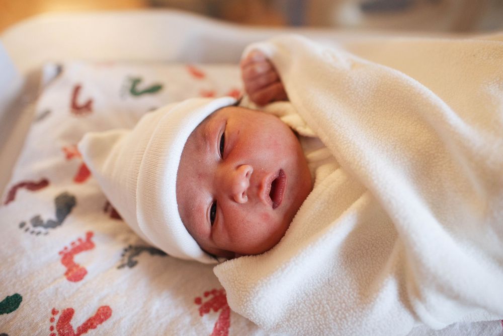 A newborn baby lays on his hospital blanket wearing a beanie and his eyes open during a Fresh 48 photo session in Seattle WA