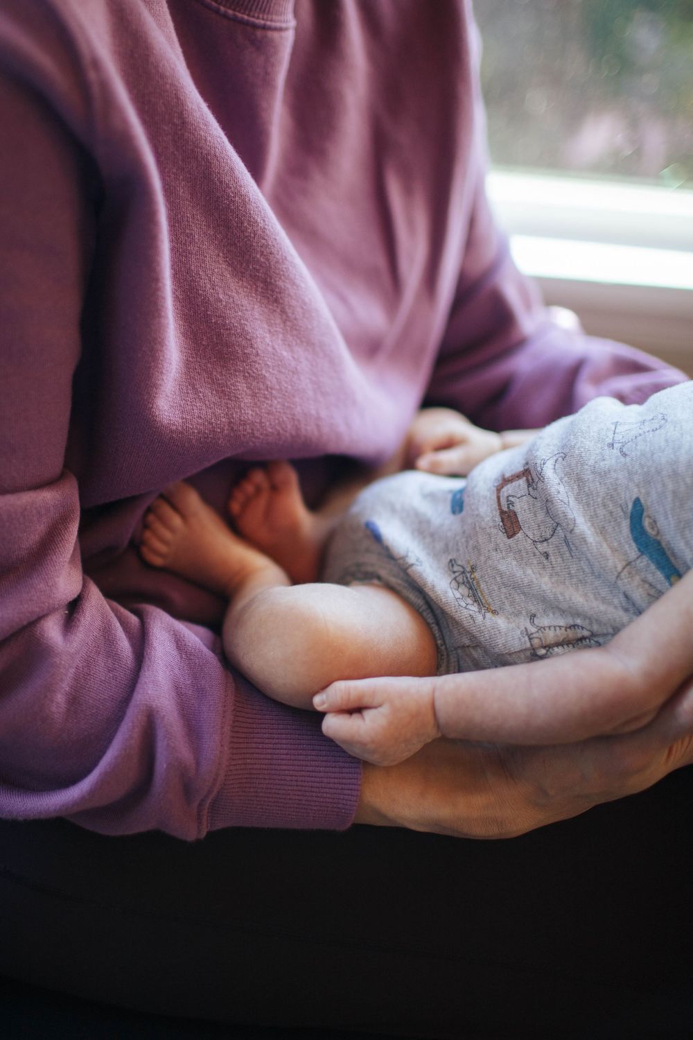 A close-up of a mother holding her baby in her lap during a newborn photo session at home in Seattle WA