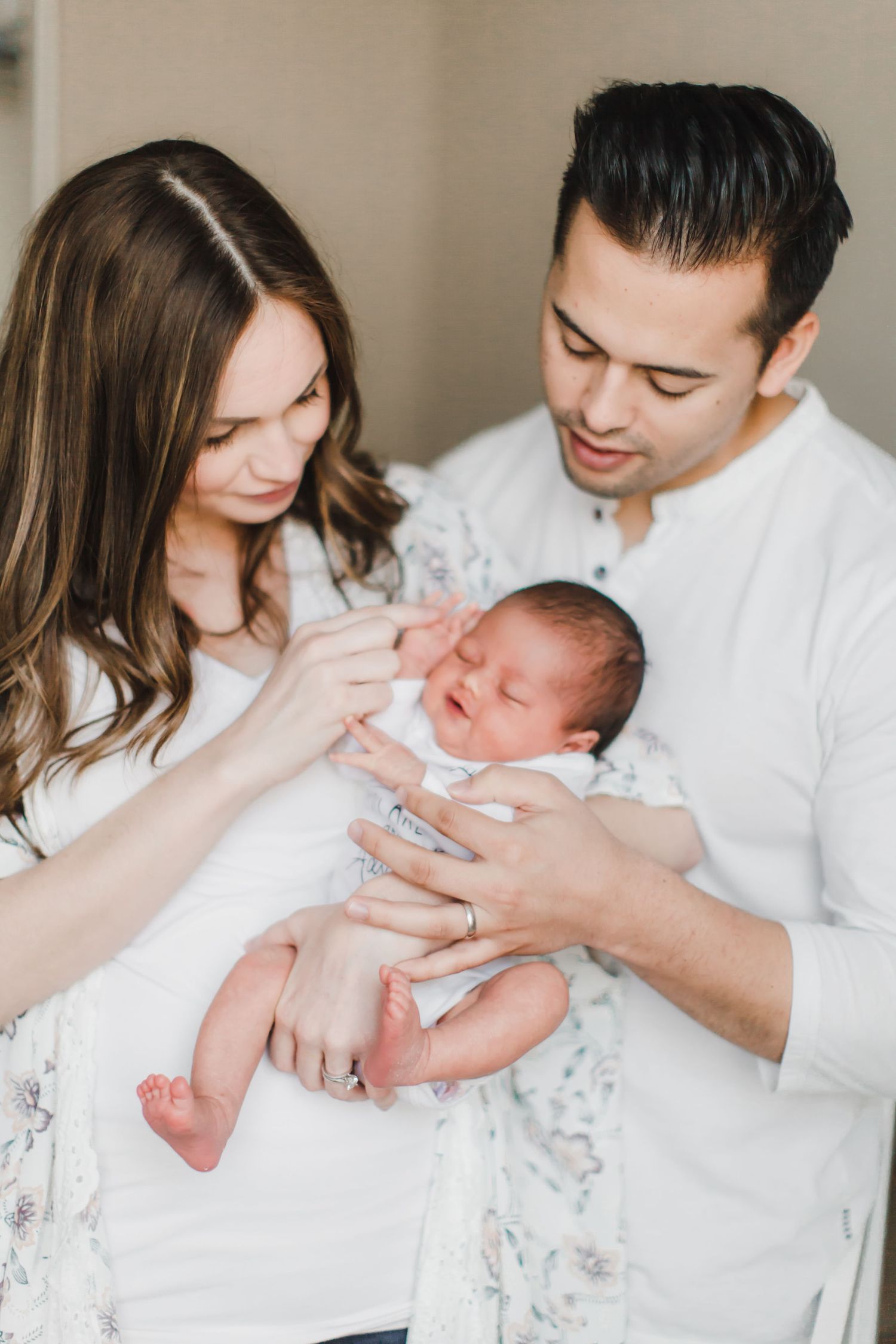 A series of intimate newborn photography shots showing tender moments between parents and their baby in white outfits.