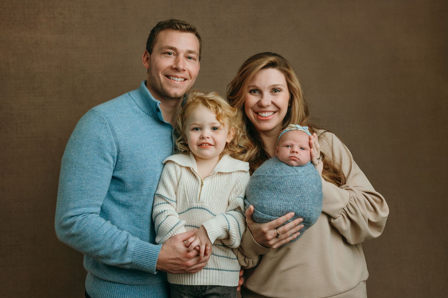 A family wearing coordinated blue and beige outfits poses together for professional portraits in a studio in Victoria BC.