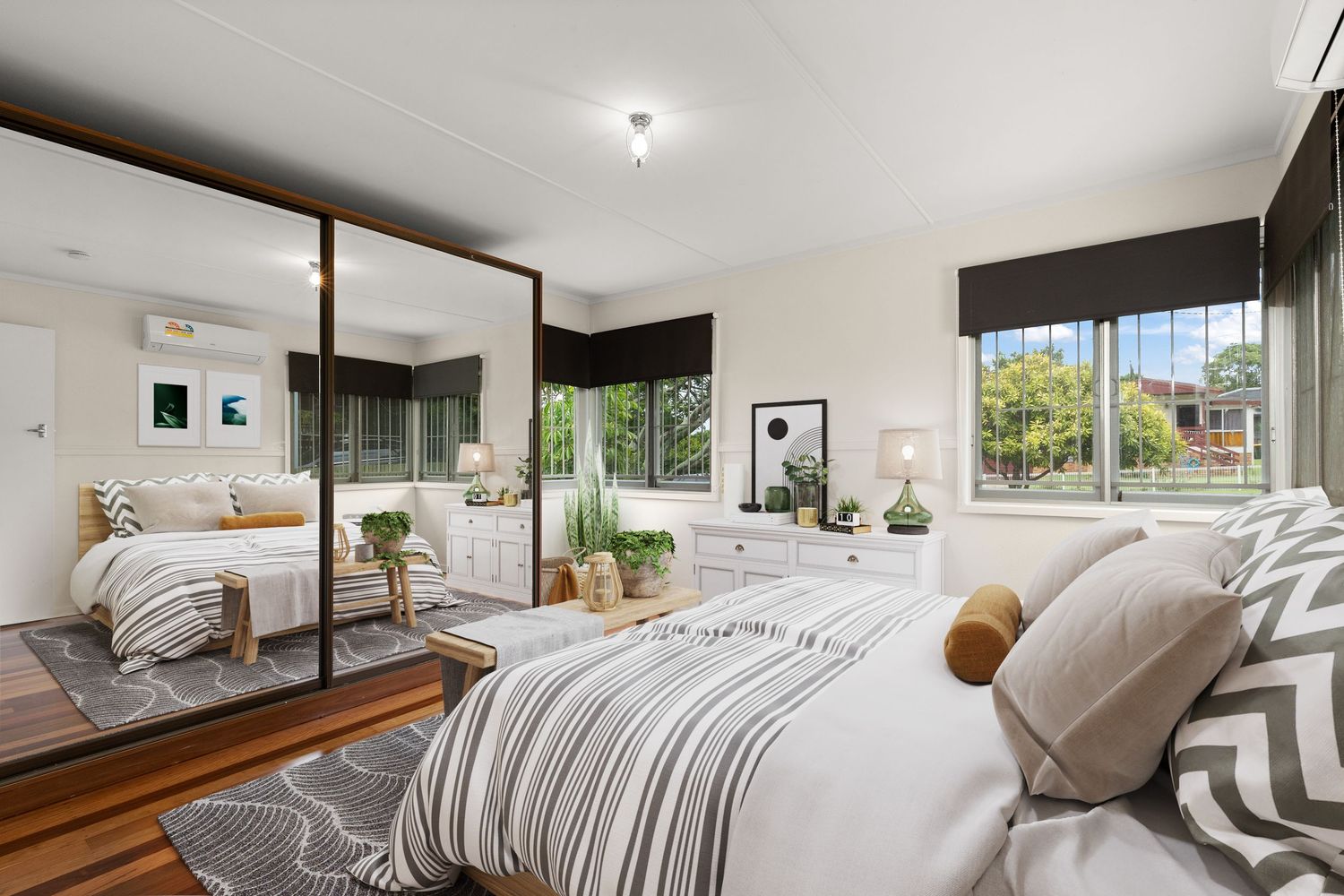 Stylish bedroom with mirrored built-in wardrobes, hardwood floors, and dual windows with garden outlook.