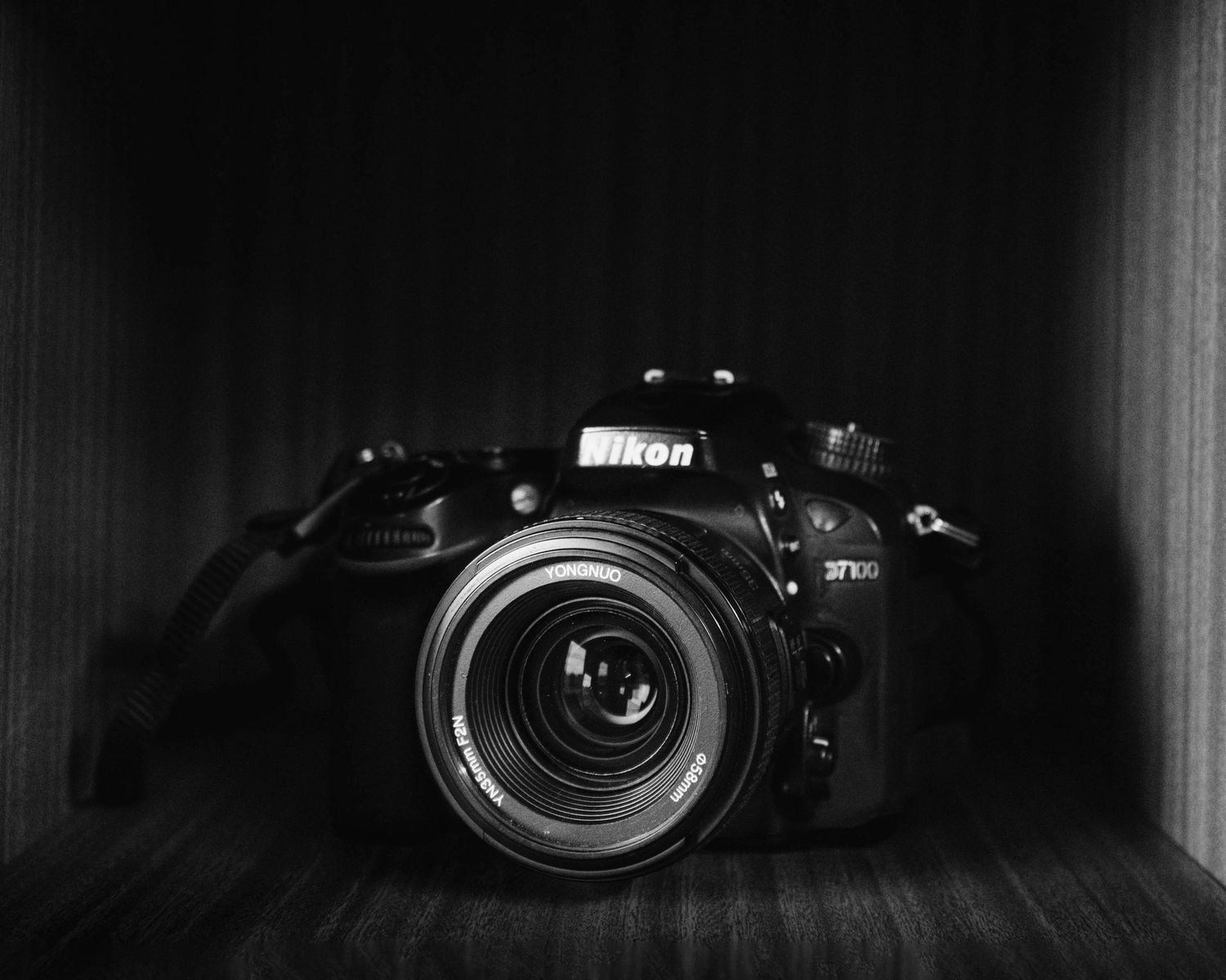 Black and white photo of a Nikon D7100 DSLR camera displayed in a wooden box.