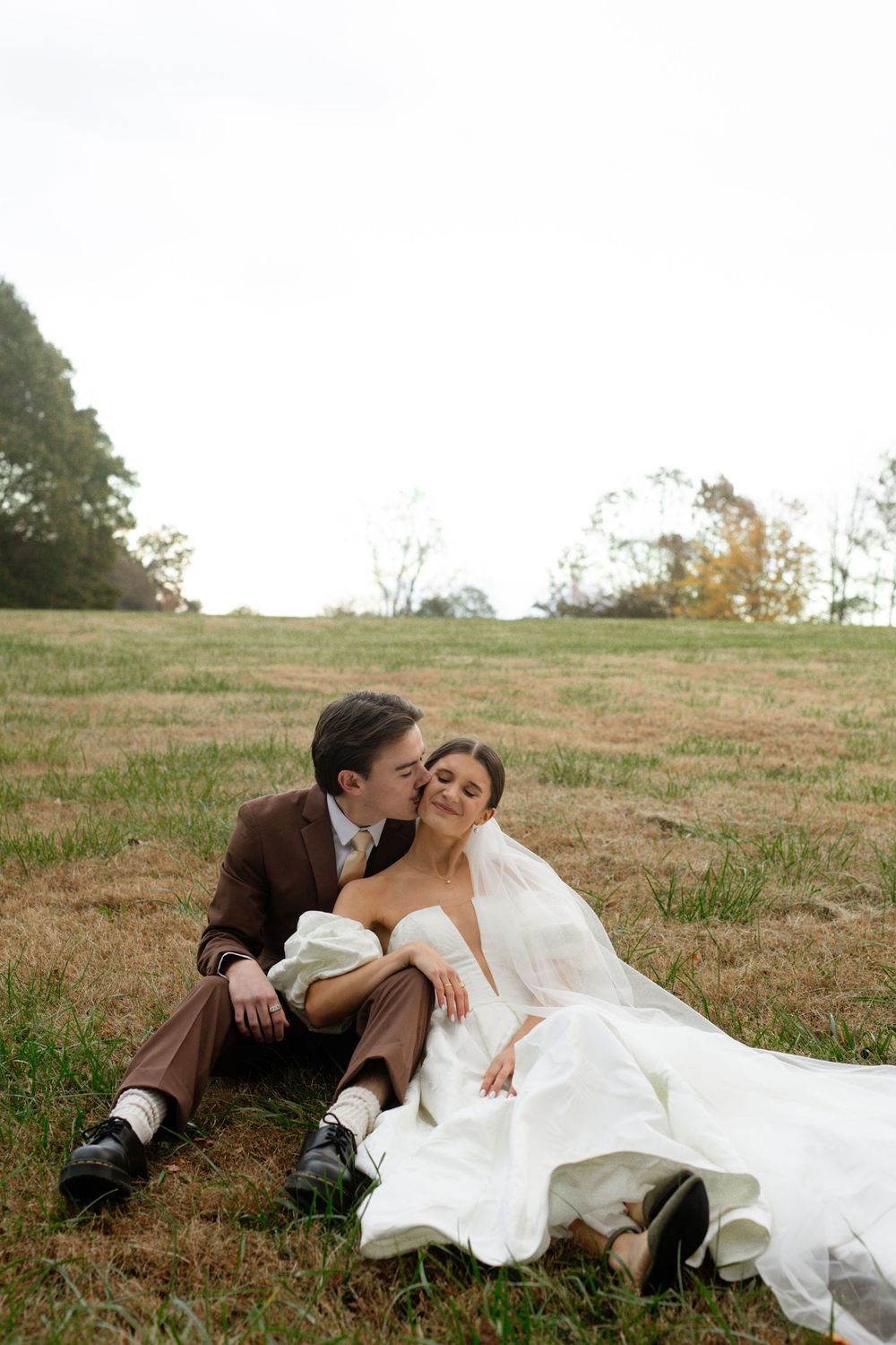 A romantic wedding photo shoot on a grassy hillside during autumn.